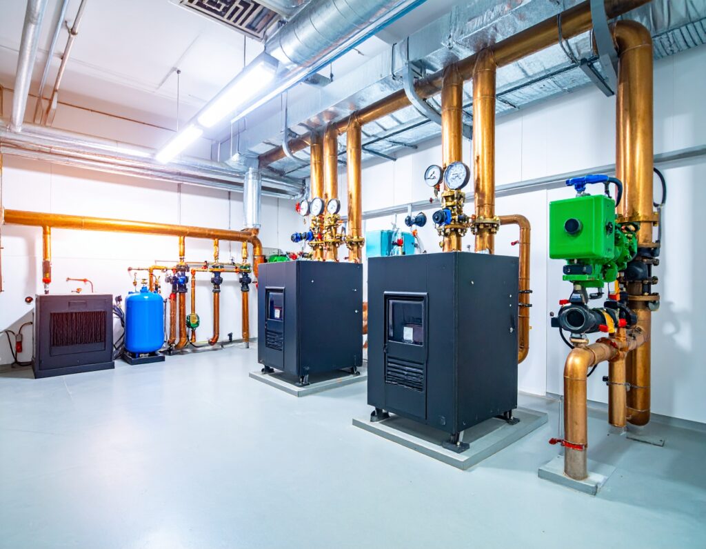 Commercial gas boiler system in a modern mechanical room with copper piping, gauges, and expansion tanks.