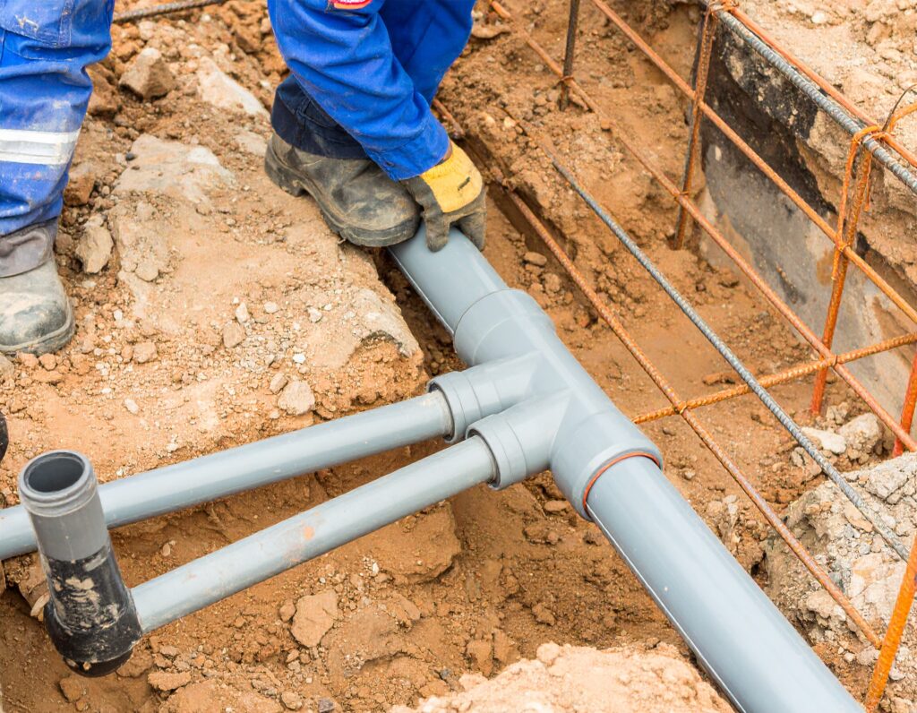 Construction worker inspecting and adjusting commercial drain pipes for cleaning and inspection during underground installation.