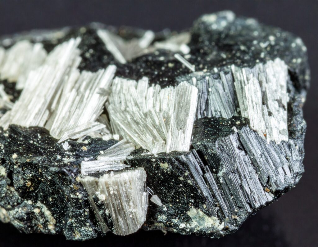 Close-up of fibrous asbestos mineral embedded in dark rock, showing sharp, needle-like white and silver fibers.