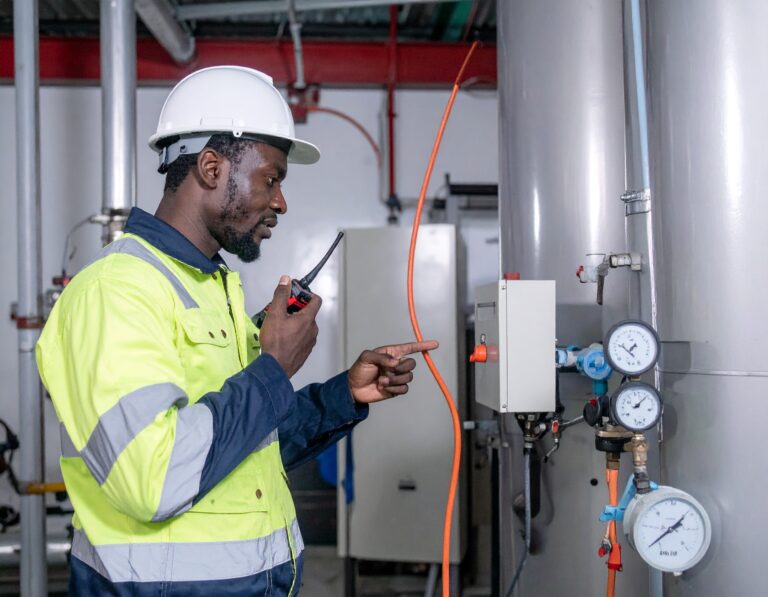 Engineer in safety gear inspecting boiler controls and gauges during gas safety check.