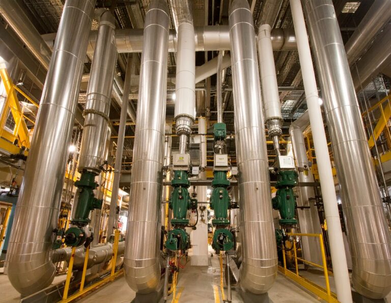 Industrial boiler room with multiple stainless steel boiler flues and green valve systems.