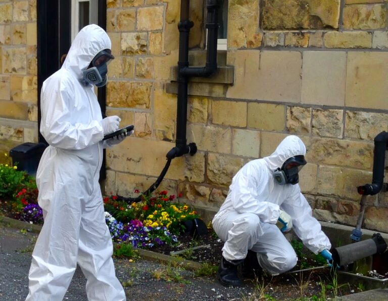Asbestos surveys and testing conducted by workers in protective suits and respirators outside a stone building.