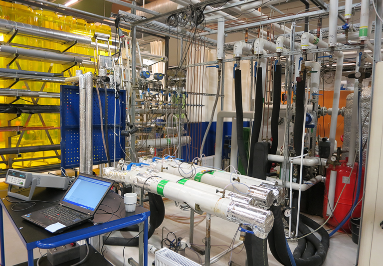 HIU testing setup showing insulated pipes, control valves, and monitoring sensors connected to a laptop for data analysis in a laboratory environment.
